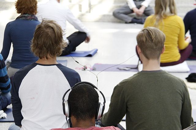 Junge Menschen sitzen in einer Halle und meditieren.