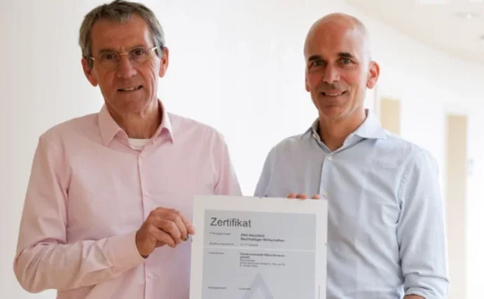 Zwei Personen halten ein Zertifikat in die Kamera.