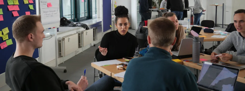 Eine Gruppe Studierender sitzt um einen Tisch herum und diskutiert.