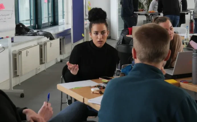 Eine Gruppe Studierender sitzt um einen Tisch herum und diskutiert.