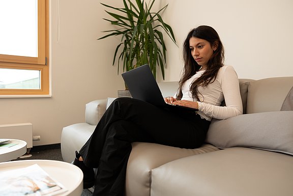 Die UW/H bietet Online-Schnupperseminare für Studieninteressierte an (Foto: UW/H I Michael Schwettmann) Foto einer jungen Frau auf einer Couch mit einem Notebook auf dem Schoß.