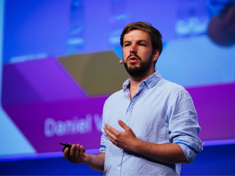 Daniel Verst steht auf einer Bühne und hält einen Vortrag.