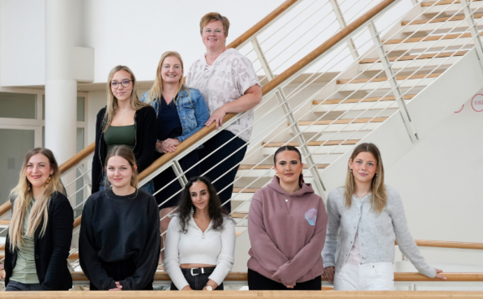 Die UW/H begrüßt einen neuen Ausbildungsjahrgang (Foto: UW/H). Gruppenfoto von neun Personen, die teils in einer Reihe, teils auf einer Treppe im Hintergrund stehen.