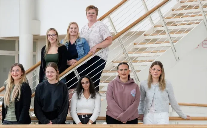 Gruppenfoto von neun Personen, die teils in einer Reihe, teils auf einer Treppe im Hintergrund stehen.