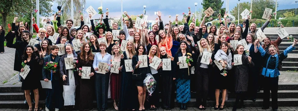 Gruppenbild von feiernden Absolvent:innen, die ihre Zeugnisse hochhalten.