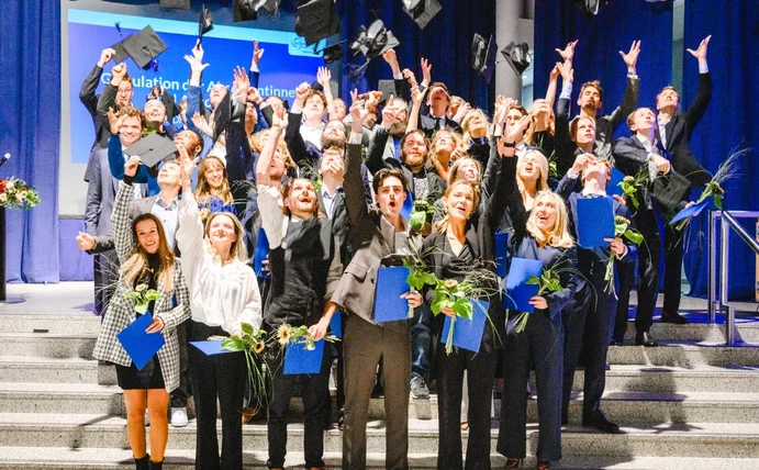 Gruppenfoto von Absolvent:innen, die ihre Hüte in die Luft werfen.