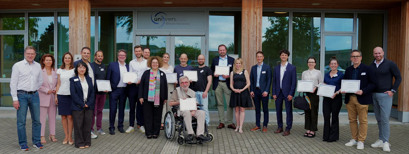 Gruppenfoto vom ATLAS-Netzwerktreffen vor dem Eingang des Holzgebäudes der Uni Witten/Herdecke.