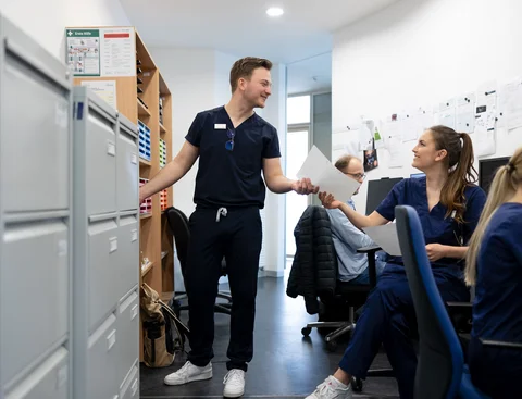 Blick in die Büroräume der Universitätszahnklinik (Foto: UW/H | Michael Schwettmann) Studierende der Zahnmedizin beschäftigen sich mit administrativen Aufgaben, arbeiten an PCs und tauschen Dokumente aus.