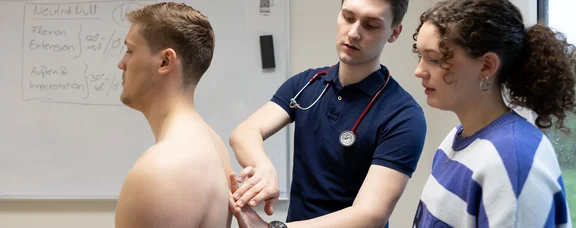 Research at the Faculty of Health at UW/H is designed to ensure sustainable healthcare. (Photo: UW/H | Michael Schwettmann) Two people stand behind a young man and treat his back.