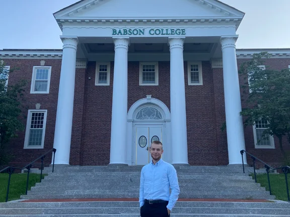 Fabian Schmidt vor dem Babson College - einem Universitätsgebäude mit Säulen vor dem Eingang.