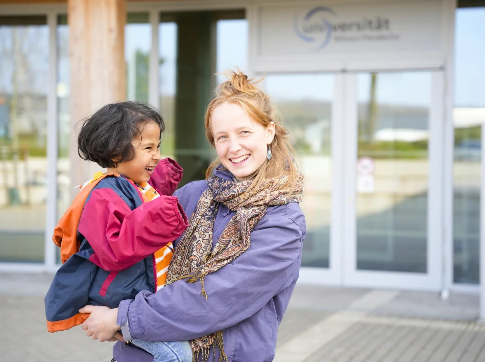 Elsa Heinsius mit Sohn Oskar vor dem Eingang des Holzgebäudes der Uni Witten/Herdecke.