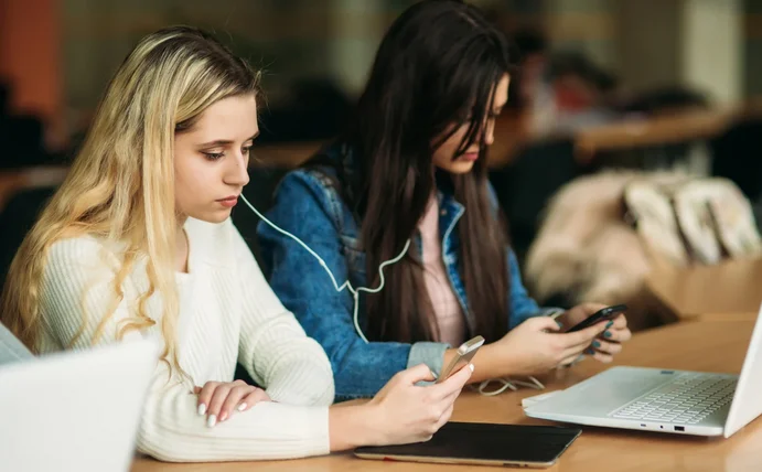 Eine Person schaut auf ihr Smartphone, eine andere auf ihren Laptop.