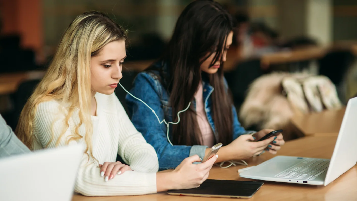 Eine Person schaut auf ihr Smartphone, eine andere auf ihren Laptop.