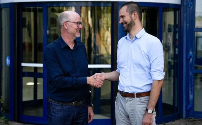 You can see the former dean, Prof. Dr. Dirk Sauerland, and the new dean, Prof. Dr. Nils-Christian Bormann, standing in front of the university's main building and shaking hands.