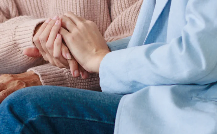 Man sieht zwei Handpaare, von einer älteren Person und von einer jüngeren Person, die Hände halten sich.