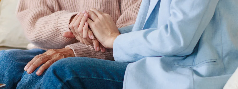 Man sieht zwei Handpaare, von einer älteren Person und von einer jüngeren Person, die Hände halten sich.