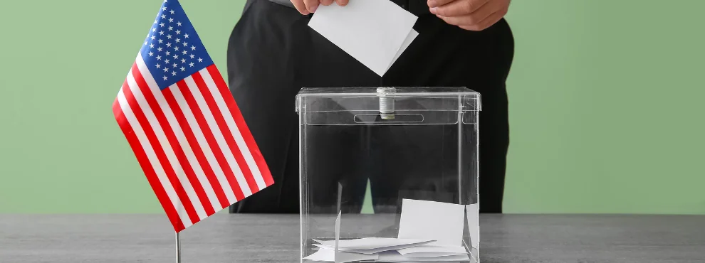 Nahaufnahme einer Wahlurne. Daneben steht eine kleine USA-Flagge.