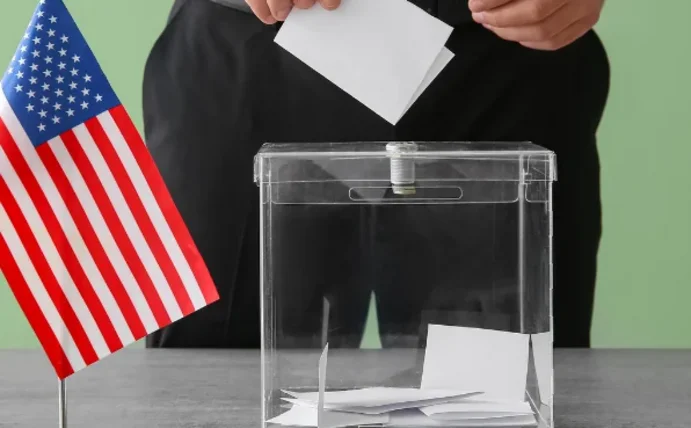 Nahaufnahme einer Wahlurne. Daneben steht eine kleine USA-Flagge.