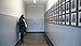 A student stands in a long corridor and looks at a wall. Portrait photos of people who were murdered in Auschwitz are hanging there.