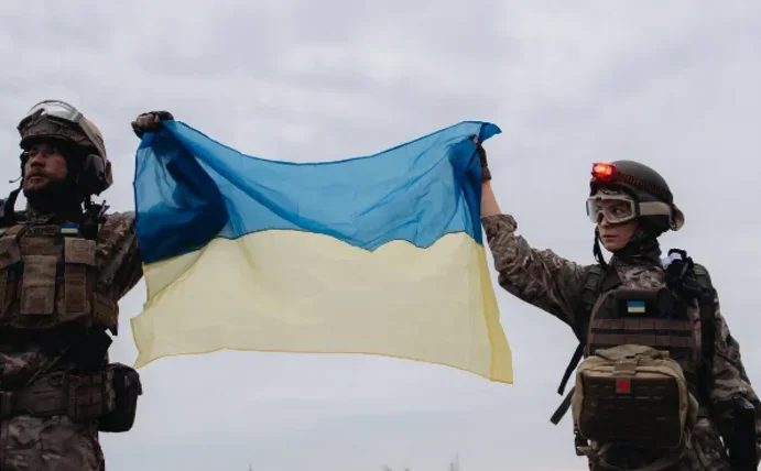 Ein Soldat links und eine Soldatin rechts halten eine Ukraineflagge in den Händen.