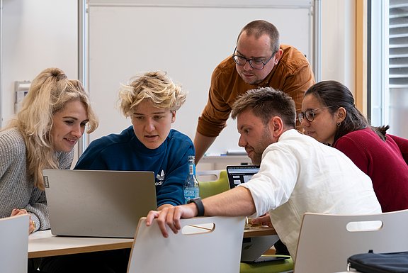 Die Summer School brachte 18 Teilnehmende aus Pflege, Psychologie, Informatik, Medizin, Ethik und angrenzenden Disziplinen an der UW/H zusammen. (Foto: UW/H | Klara Schmickler) Fünf Personen schauen gemeinsam auf einen Laptop.