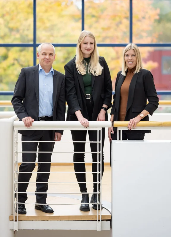 Das Team des Lehrstuhls für Marketing steht im Innenraum an einem Geländer