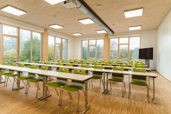 Seminar room in the wooden building of the UW/H (Photo: UW/H | Johannes Buldmann) Interior shot of a brightly lit seminar room with rows of tables and chairs