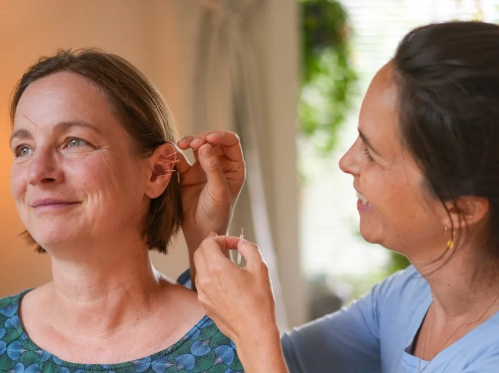 A doctor is treating a woman with ear acupuncture.