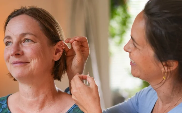 A doctor is treating a woman with ear acupuncture.