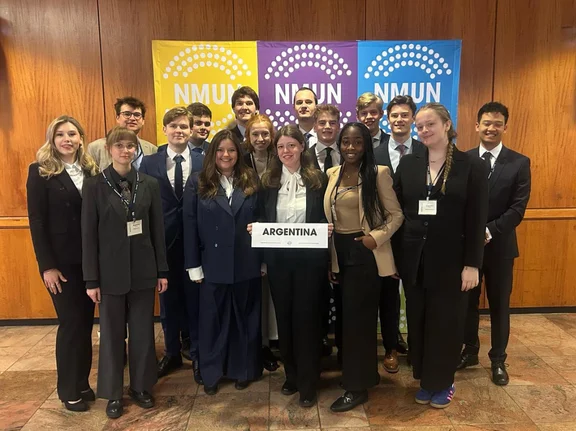 Gruppenfoto von Studierenden in formeller Kleidung vor einer bunten Wand.