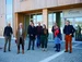A group of people stand in front of the UW/H wooden building.