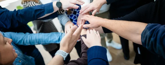 Teilnehmer im Lehrgang legen die Hände aufeinander.