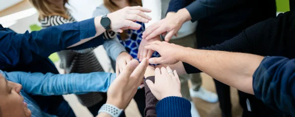 Teilnehmer im Lehrgang legen die Hände aufeinander.