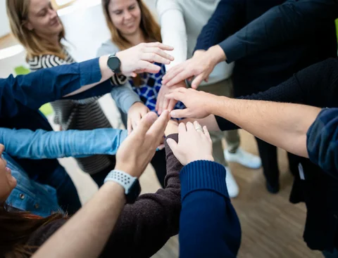 Teilnehmer im Lehrgang legen die Hände aufeinander.