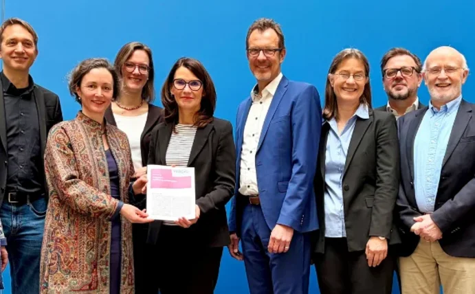 Zehn Menschen stehen vor einem blauen Huntergrund. Zwei Frauen halten eine Urkunde fest. Übergabe der Lagebeurteilung an die Parlamentarische Staatssekretärin Rita Schwarzelühr-Sutter im Bundesumeweltministerium.