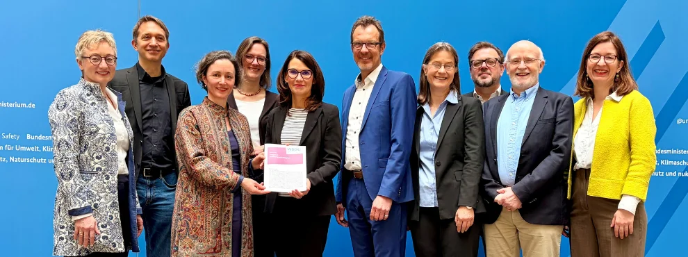 Zehn Menschen stehen vor einem blauen Huntergrund. Zwei Frauen halten eine Urkunde fest. Übergabe der Lagebeurteilung an die Parlamentarische Staatssekretärin Rita Schwarzelühr-Sutter im Bundesumeweltministerium.