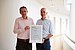 Two people hold a certificate up to the camera.