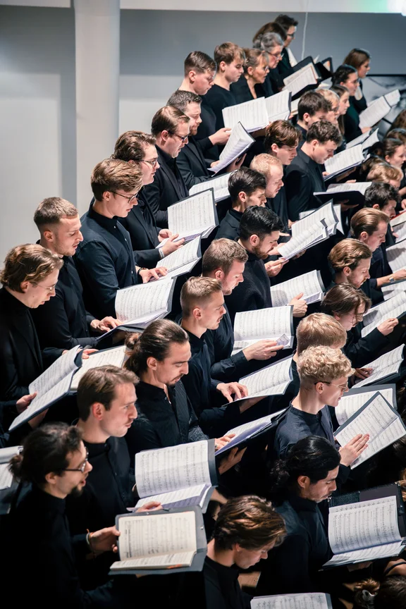 Photo of a choir with several singers holding sheet music in their hands.