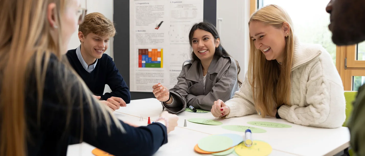 Lerne unsere Psychologie-Studiengänge kennen als Student:in fü einen Tag. (Foto: UW/H | Michael Schwettmann) Eine Gruppe junger Menschen sitzt an einem Tisch und arbeitet zusammen.