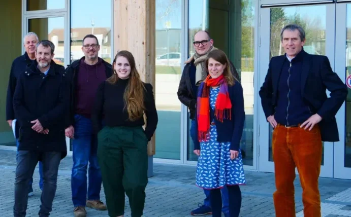 Eine Gruppe Personen steht vor dem Holzgebäude der UW/H.