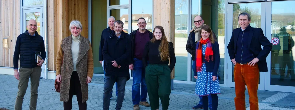 A group of people stand in front of the UW/H wooden building.