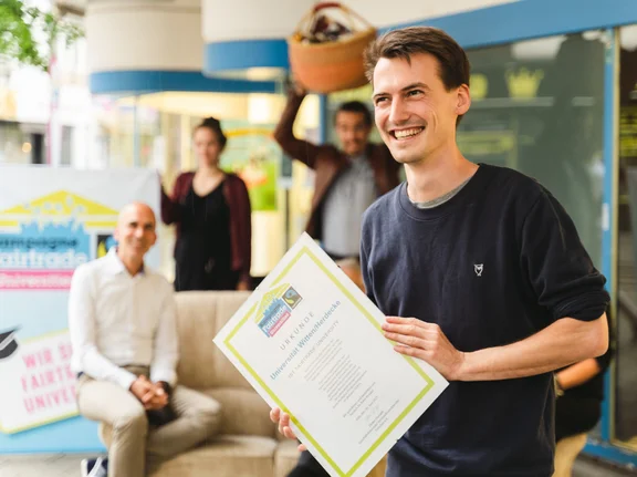 Domenik freut sich, dass die UW/H als erste Uni im Ruhrgebiet den Fairtrade-Titel bekommt. (Foto: UW/H | Johannes Buldmann) Domenik hält freudestrahlend die Fairtrade-Urkunde in der Hand