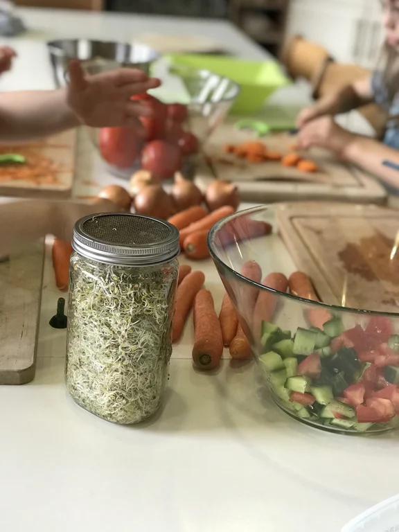 Ein Glas mit Sprossen steht neben einer Schüssel mit Gemüse.