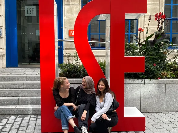 Drei junge Frauen sitzen auf einer Skulptur aus Buchstaben.