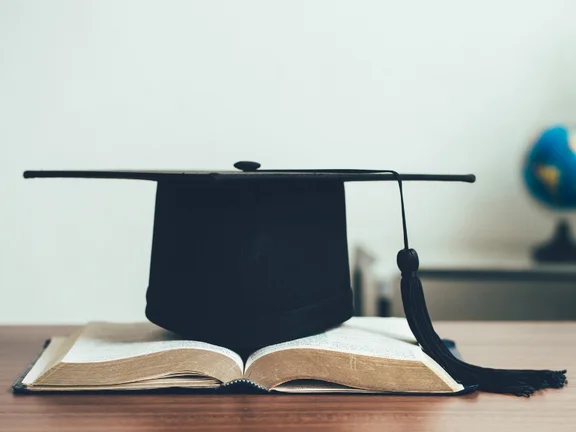 A PhD at UW/H paves the way for a career in academia. (Photo: Canva) A doctoral cap is resting on an open book.