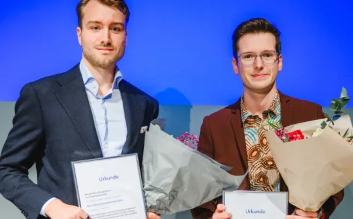 Niklas Kaminski und Nicolas Schweer haben je einen Blumenstrauß und eine Urkunde in der Hand und lächeln in die Kamera.