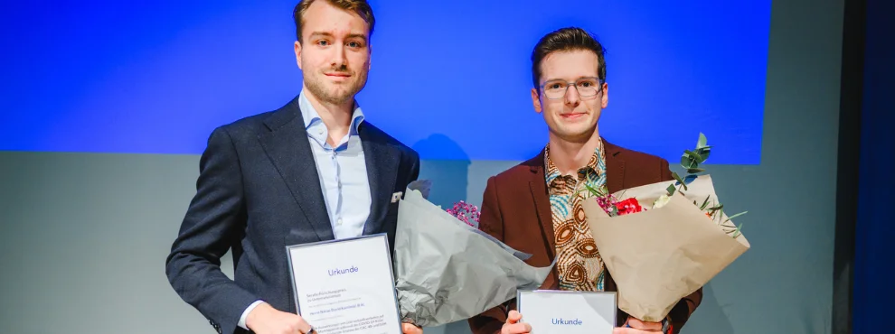 Niklas Kaminski und Nicolas Schweer haben je einen Blumenstrauß und eine Urkunde in der Hand und lächeln in die Kamera.