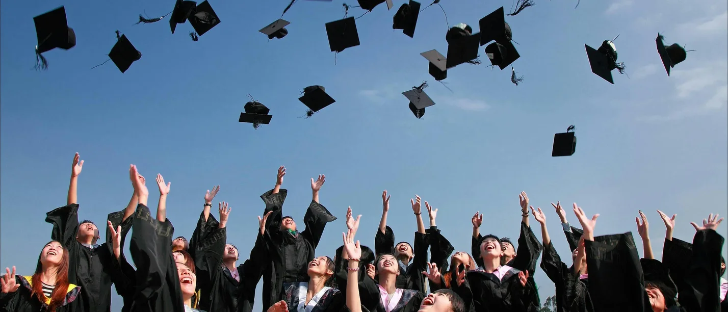 Eine Gruppe von Absolvent:innen wirft ihre Absolvent:innen-Kappen in die Luft.