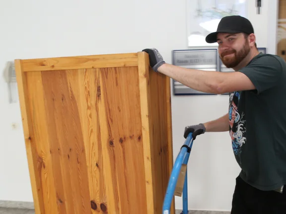  Andreas transportiert einen Schrank mit einer Lastkarre.