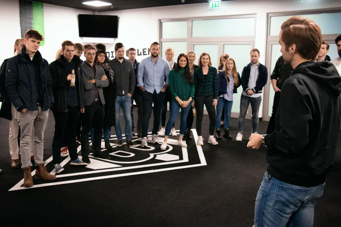 A visit to Borussia Mönchengladbach. (Photo: UW/H │ Linda Lösser) A group photo of students in a meeting room. The logo of the Borussia Mönchengladbach football club can be seen on the floor.